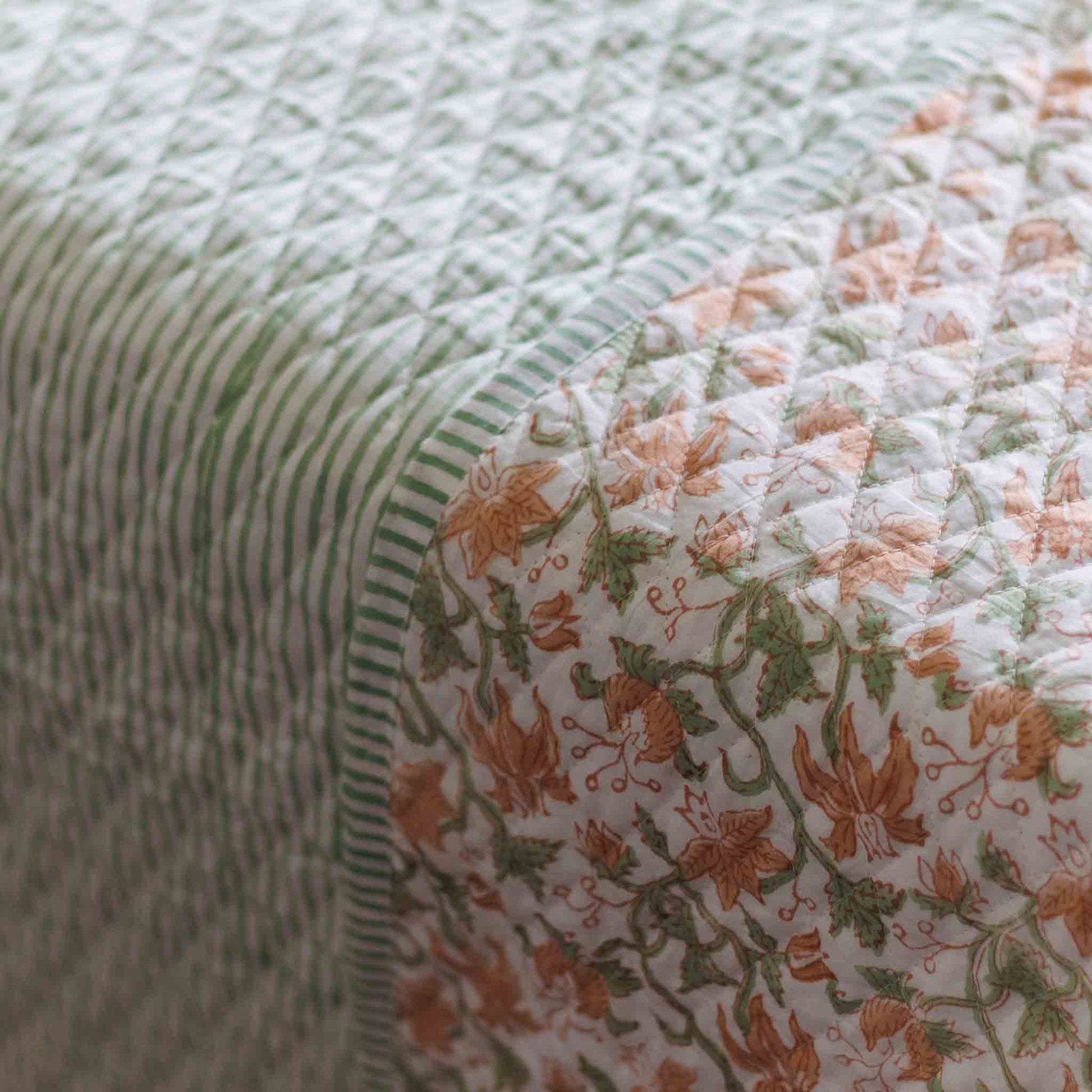 Close-up of a quilted fabric with a striped green and white side and a floral side in peach, green, and white, showing the diamond-quilted texture.