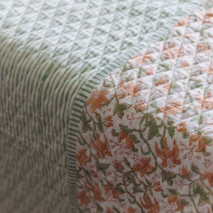 Close-up of a quilted fabric with a striped green and white side and a floral side in peach, green, and white, showing the diamond-quilted texture.