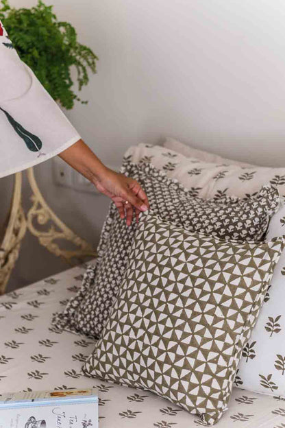 Person arranging printed cushions on a bed with a plant in the background