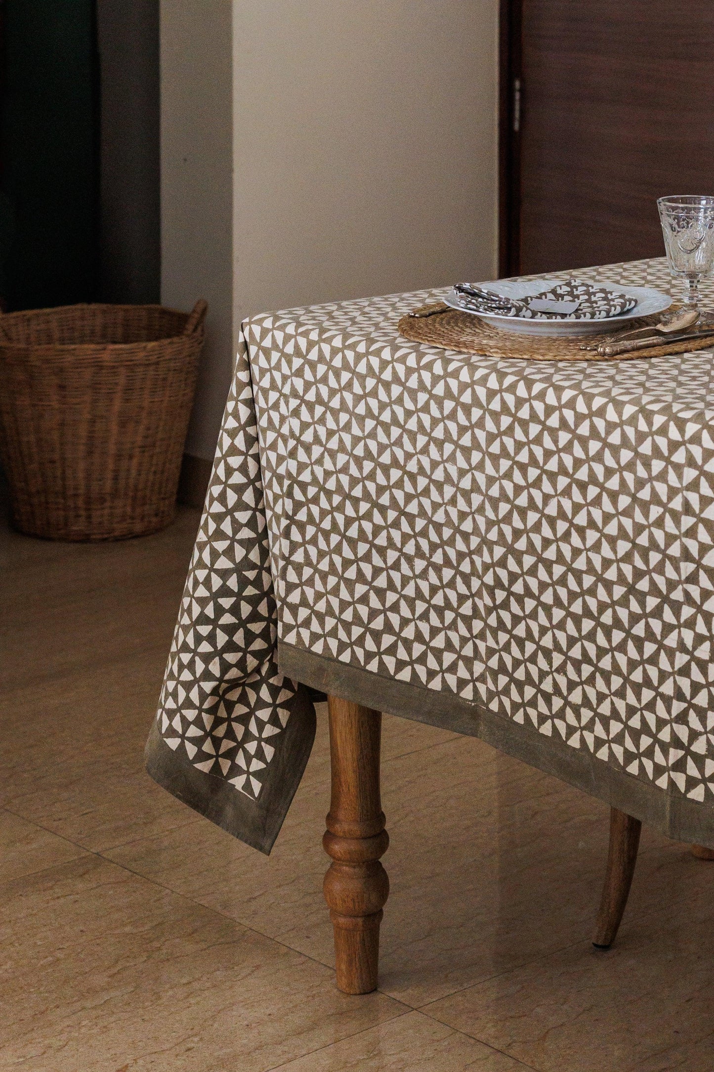 Table with a patterned tablecloth in a room with a basket and wooden door.