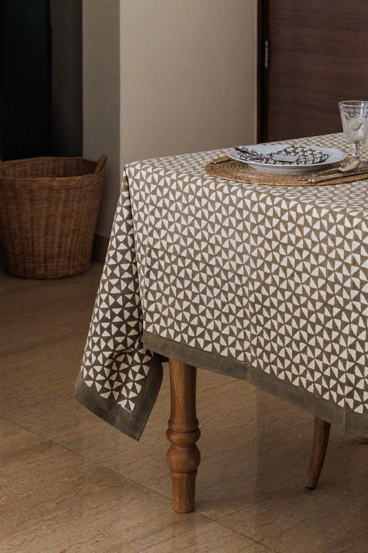 Table with a patterned tablecloth in a room with a basket and wooden door.