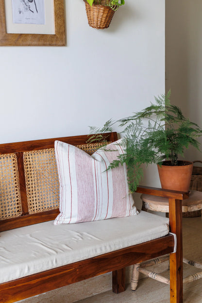 Wooden bench with striped cushions and a plant on a white wall.