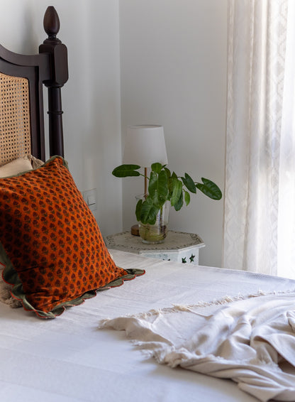 Bedroom with orange cushion, white bedding, and a small table with a plant.