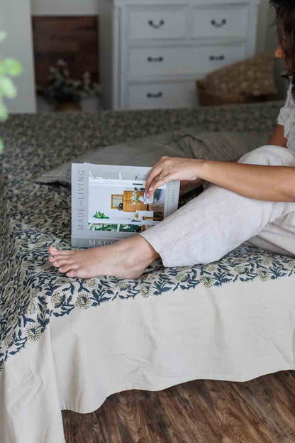 A person sitting on a bed reading a book with a blue floral block print bed sheet and pillowcases in a matching colour palette.