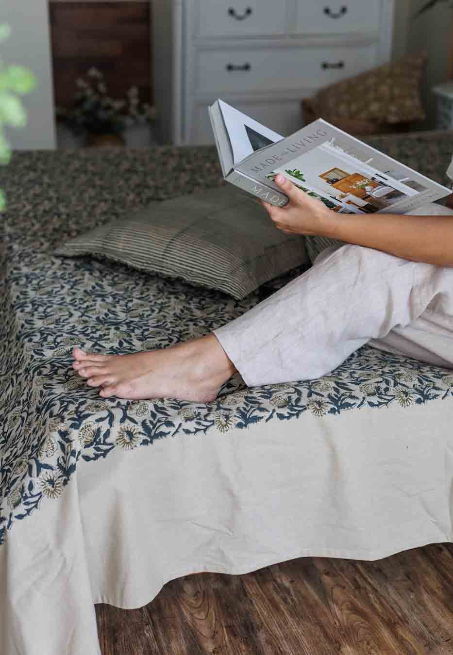 A person sitting on a bed reading a book with a block print bed sheet and pillowcases in a matching colour palette.