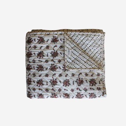A block print quilted bedspread in a cream base, featuring a dark brown floral pattern on one side and polka-dot pattern on the other. 