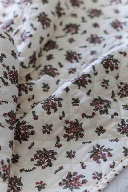 A close-up of a quilted fabric with an off-white background and a repeating floral pattern in dark green and muted red.