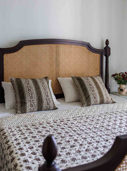 A bed room featuring a bed decorated with a quilted block print bedspread and two floral block print cushion covers
