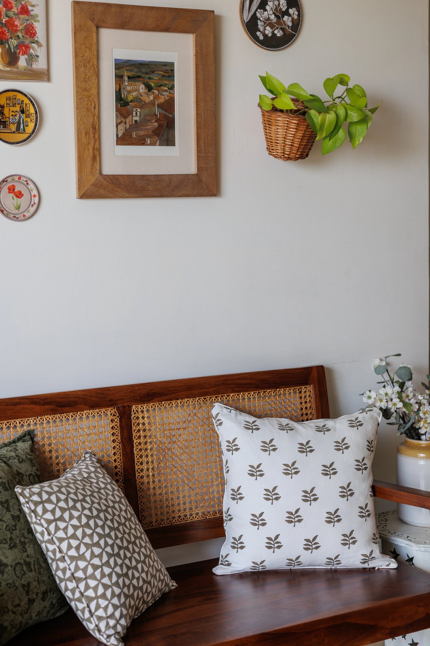 Decorative pillows on a wooden bench with wall art and plants in the background