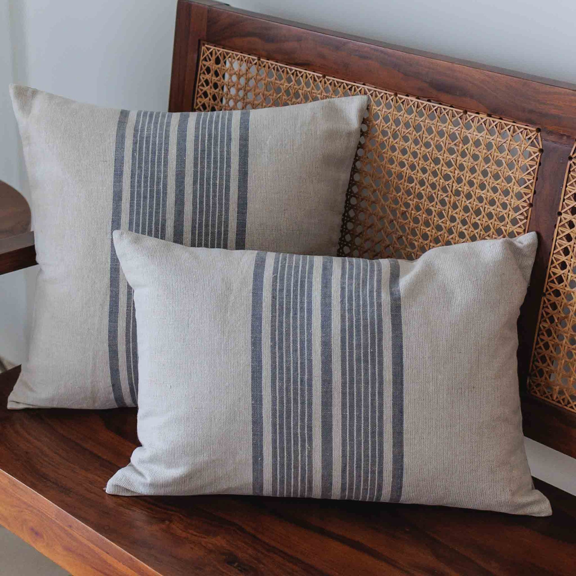 Two striped pillows on a wooden bench with a wicker backrest.