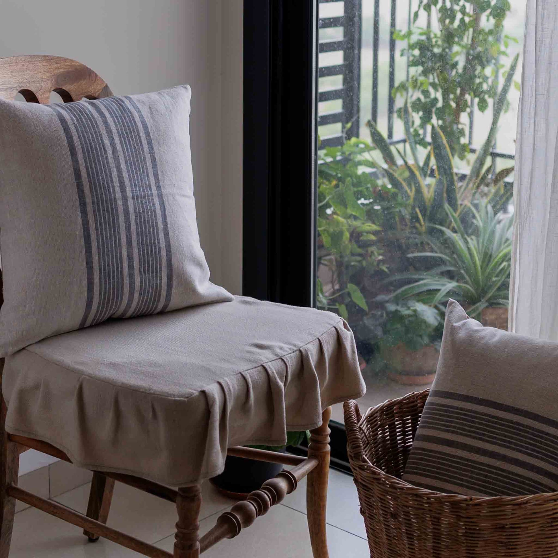Chair with striped linen pillow, wicker basket with striped pillow, plants in the background
