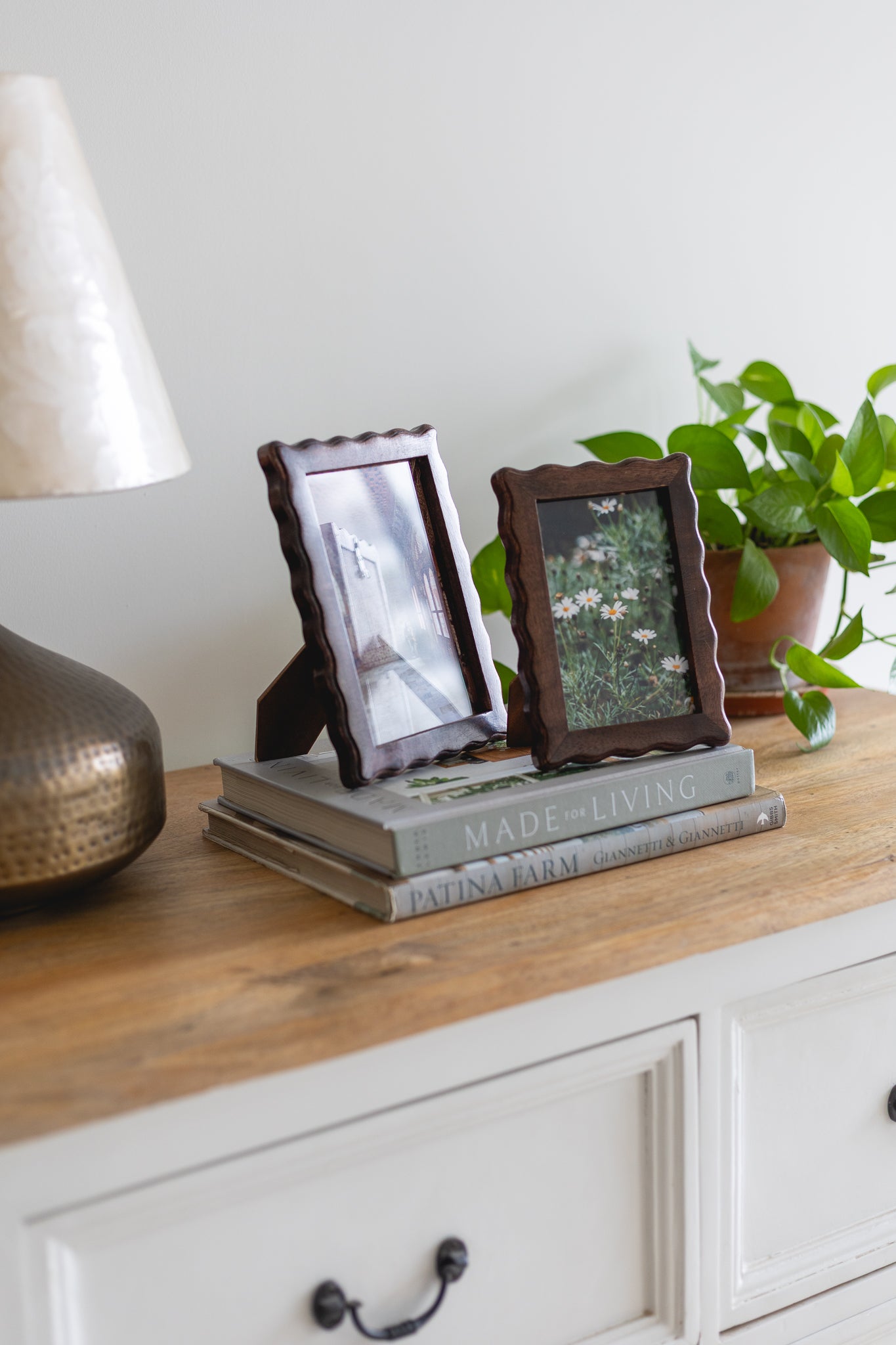 Two wooden picture frames on a stack of books with a lamp and plant in the background.
