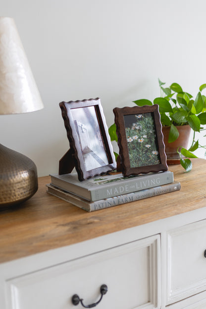 Two wooden picture frames on a stack of books with a lamp and plant in the background.