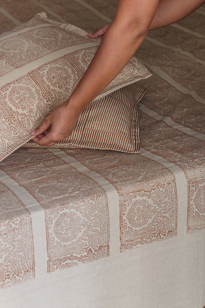 A person is laying on a bed with a beige and brown block printed cotton bedsheet with pillowcase.