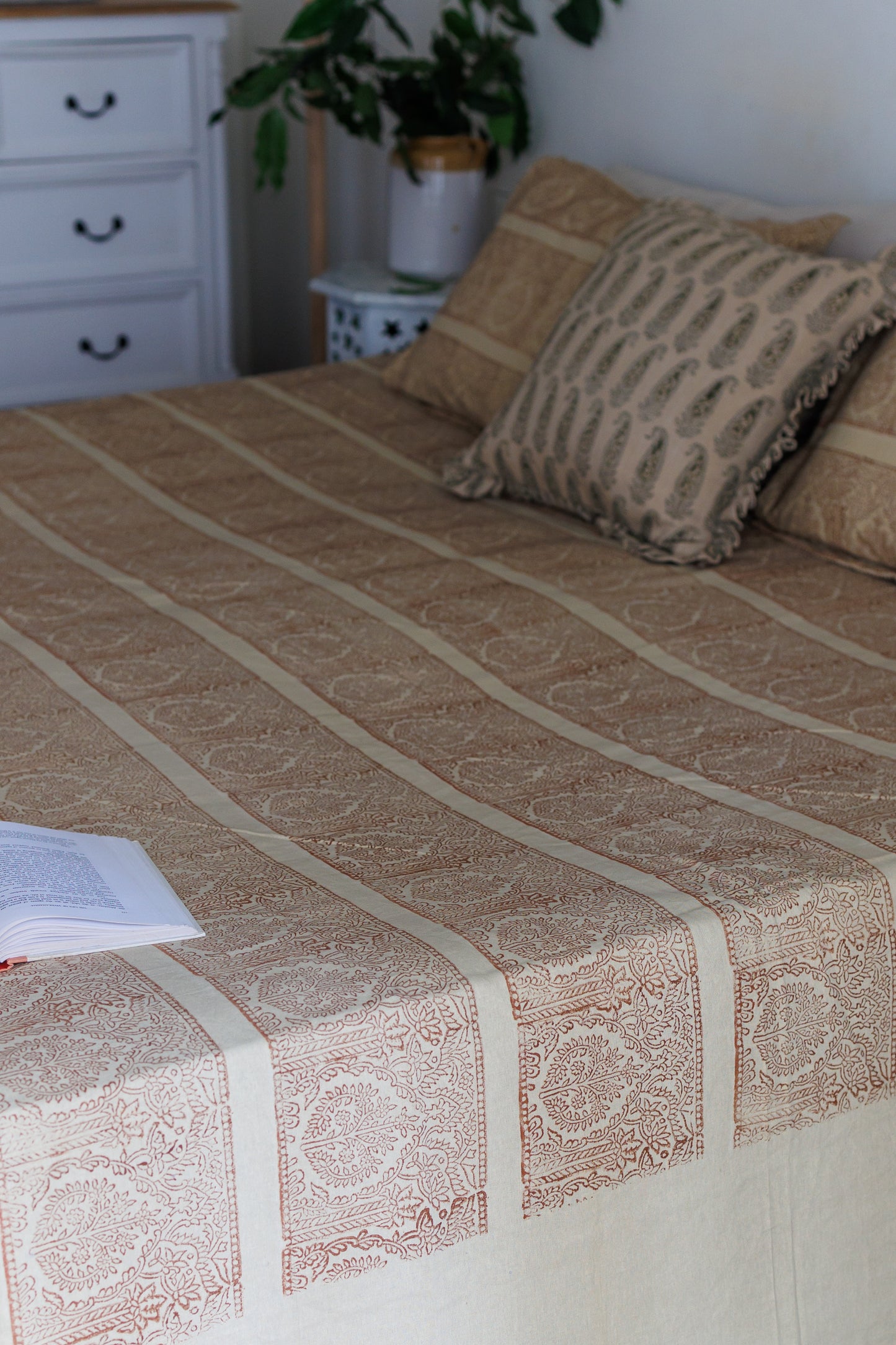 A  bed with a beige and brown block printed cotton bedsheet and pillowcase.