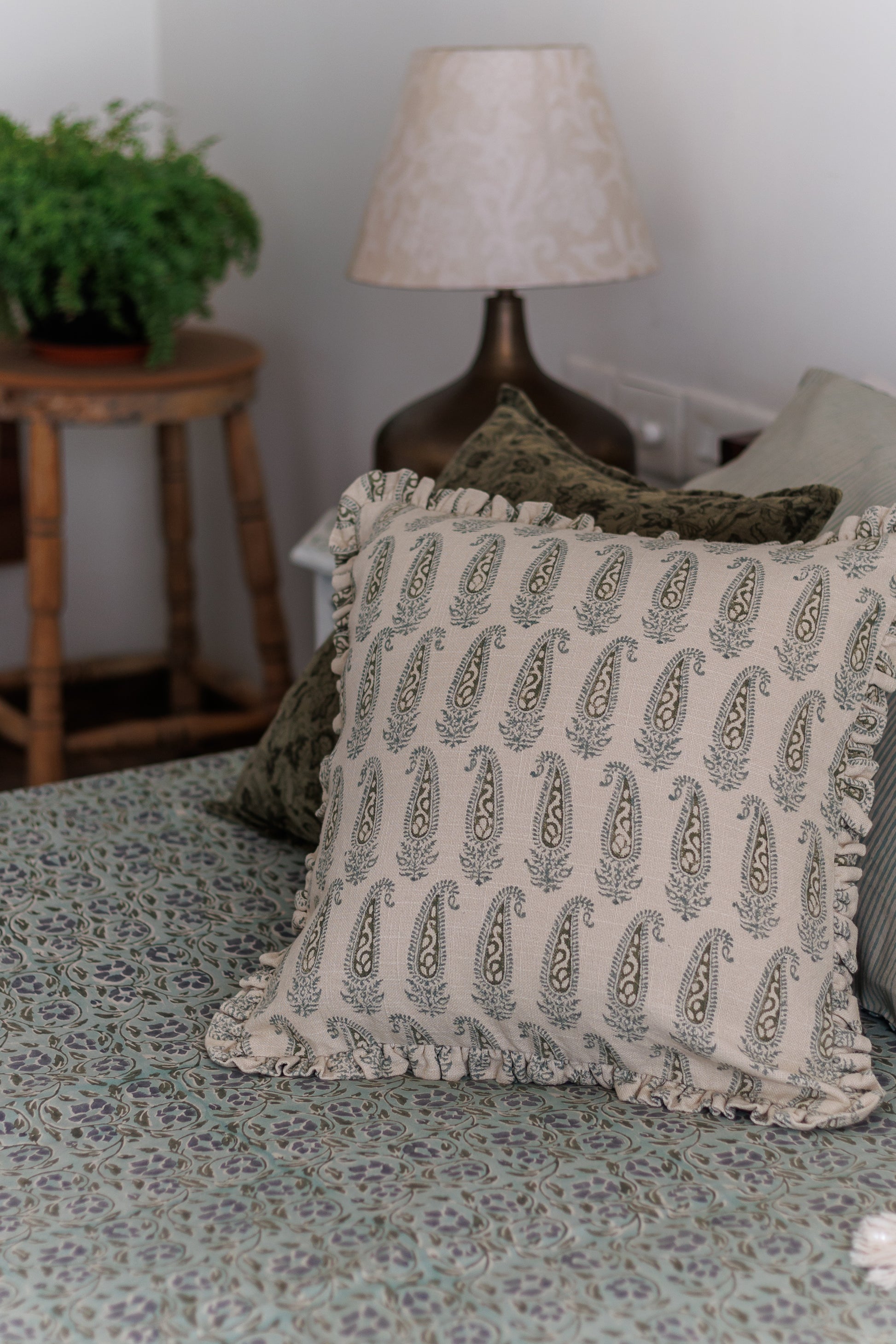 A cushion cover with a paisley block print pattern in shades of green, featuring ruffles and placed on a bed