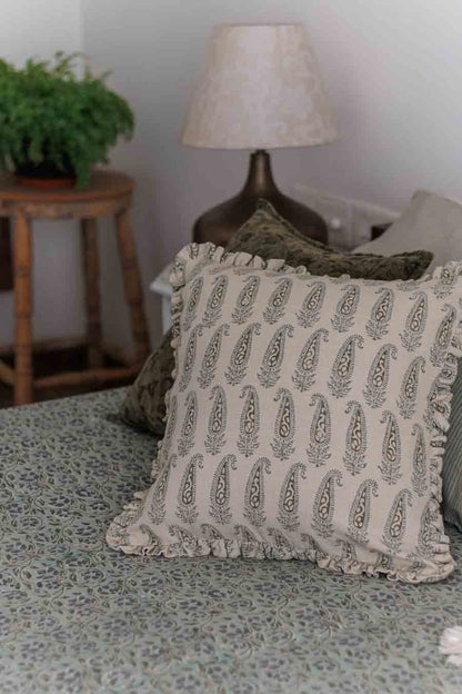 A cushion cover with a paisley block print pattern in shades of green, featuring ruffles and placed on a bed
