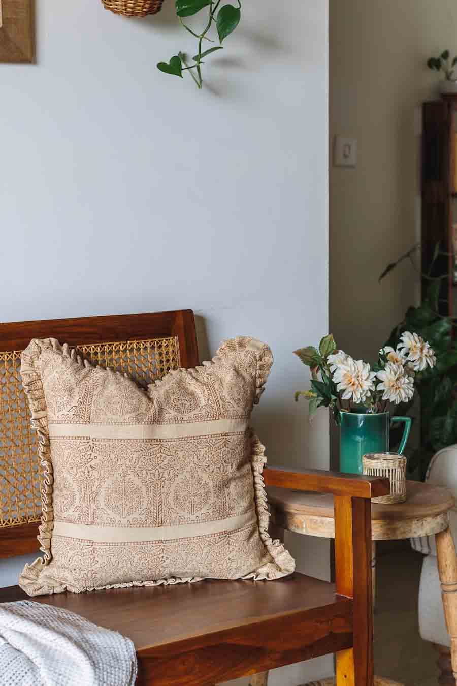Rust Block print cushion with ruffled edges resting on a wooden armchair in a styled room setting. 
