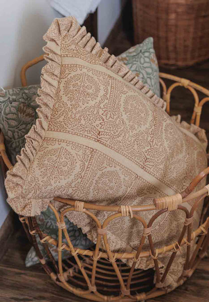 A rust patterned lumbar cushion with a ruffled edge sits in a woven rattan basket.