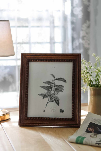 Framed botanical print on a table with a lamp and plant in the background