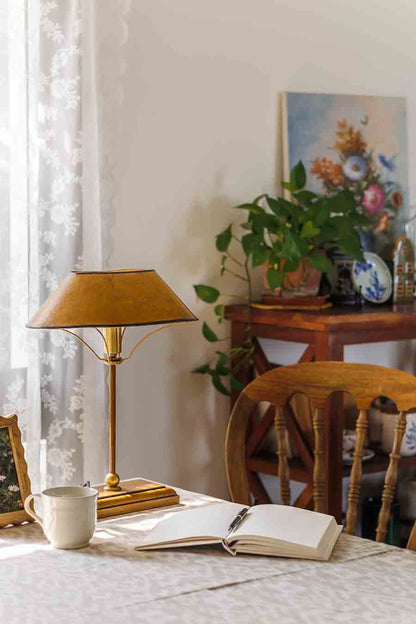 Home office setup with a brass study lamp, open book, and cup on a desk.