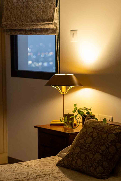 A warm, cozy bedroom scene featuring a lit table lamp on a nightstand, next to a bed with a patterned pillow.