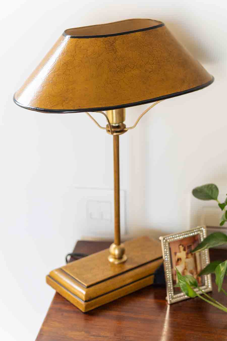 A vintage-style table lamp with a textured gold metal shade, a brass stem,  styled on a wooden table.