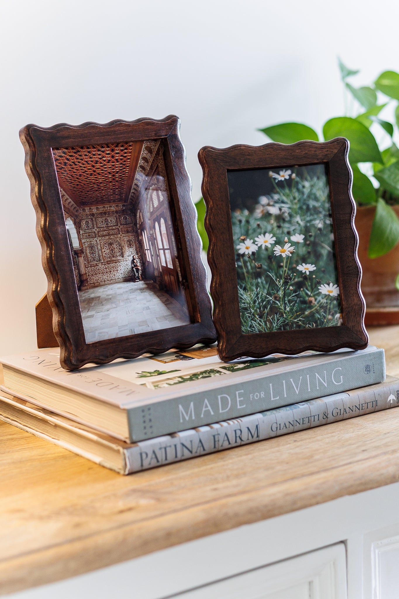 Two wooden picture frames with photos on top of books on a wooden surface.