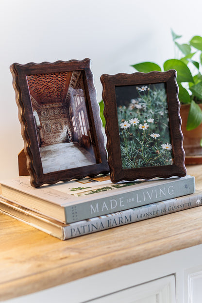 Two wooden picture frames with photos on top of books on a wooden surface.